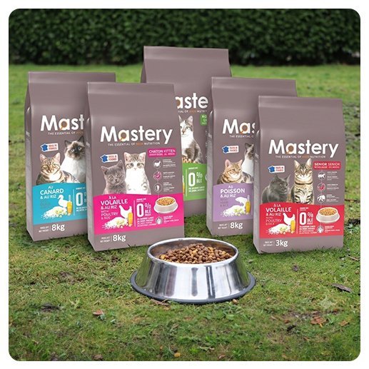Les sacs de croquettes Mastery pour chat posés dans l'herbe autour d'une gamelle (visuel officiel)