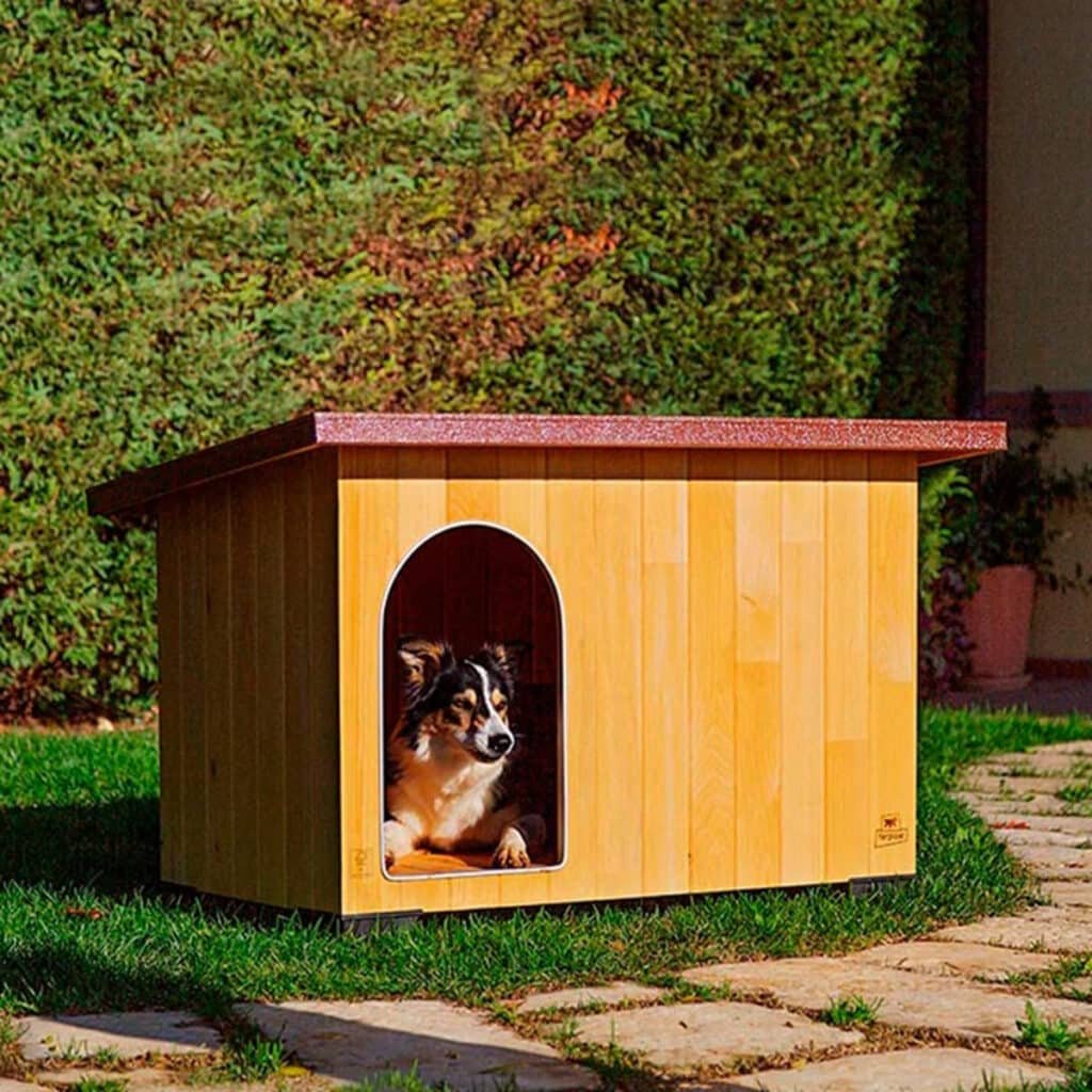 Chien couché à l'entrée de la niche Ferplast Baita dans un jardin